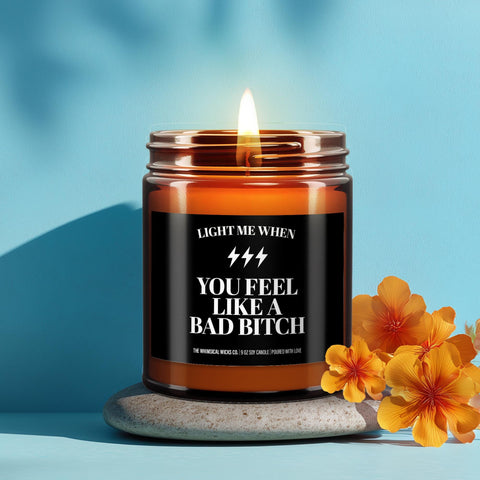 Funny candle with pink label that reads βYou Feel Like a Bad Bitchβ in bold yellow text, set on a stone with dried flowers and a cozy living room vibe. Perfect self-love or confidence-boosting gift for her. Aesthetic lifestyle shot designed to appeal to shoppers looking for empowering, sassy candles and funny gift ideas for women.
