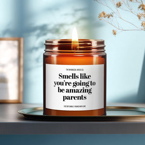 9oz amber glass soy candle with “Smells like you’re going to be amazing parents” label, lit and placed on a soft teal ceramic tray. Minimalist setting with warm sunlight and gentle shadows, styled for cozy, modern gift presentation.