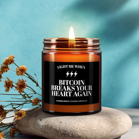 Amber jar candle with label that reads βLight me when Bitcoin breaks your heart again,β lit and styled with lavender and citrus on a bright blue background.