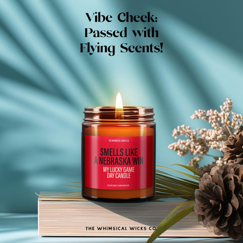Candle lit and glowing, with the red label saying “Smells Like A Nebraska Win – My Lucky Game Day Candle.” Surrounded by dried florals, pinecones, and playful lighting. A cozy, humorous candle for college football lovers, ideal for tailgates, dorm rooms, and win-day rituals.