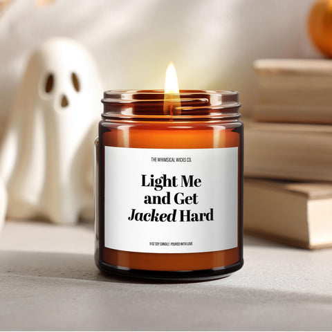 Close-up of a 9oz amber glass jar candle with black metal lid, white label reading “Light Me and Get Jacked Hard” in bold black text, styled on a neutral background with warm lighting, perfect for outrageous adult Halloween gifting.