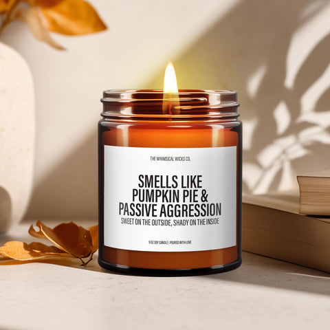 Close-up of a 9oz amber glass jar candle with black metal lid, white label reading “Smells Like Pumpkin Pie and Passive Aggression – Sweet on the outside, shady on the inside” in bold black text, styled on a neutral background with warm lighting, perfect for cheeky Thanksgiving gifting.