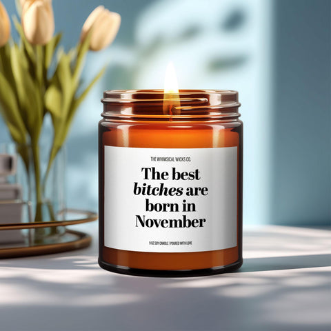 Close-up of a 9oz amber glass jar candle with black metal lid, white label reading “The Best Bitches Are Born in November” in bold black text, styled on a neutral background with warm lighting, perfect for cheeky November birthday gifting.