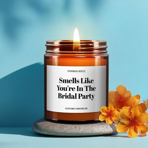 Amber jar candle with label that reads “Smells Like You’re in the Bridal Party,” lit and styled with lavender and citrus on a bright blue background.
