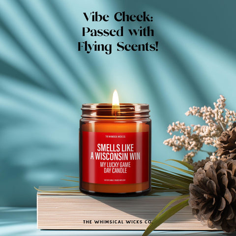 Candle lit with a cozy flame, label reading “Smells Like A Wisconsin Win – My Lucky Game Day Candle.” Set on stacked books with pinecones and dried florals, blue background with spotlight effect. Ideal gift for college football lovers and Wisconsin supporters. Warm sporty vibes, great for celebration moments.