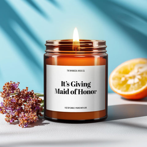 Amber jar candle with label that reads “It’s Giving Maid of Honor,” lit and styled with lavender and citrus on a bright blue background.