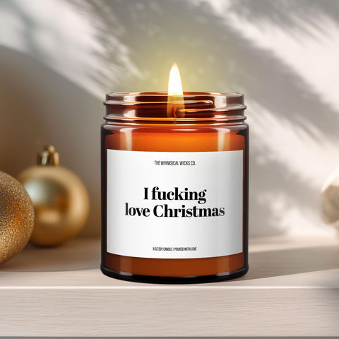 Close-up of a 9oz amber glass jar candle with black metal lid, white label reading “I Fucking Love Christmas” in bold black text, styled on a neutral background with warm lighting, perfect for bold and humorous holiday gifting.