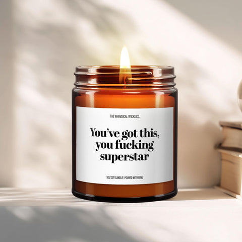 Close-up of a 9oz amber glass jar candle with black metal lid, white label reading “You’ve Got This You Fucking Superstar” in bold black text, styled on a neutral background with warm lighting, perfect for motivational and cheeky gifting.