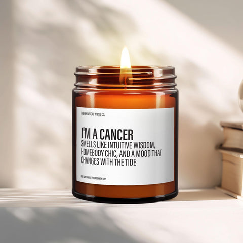 Amber glass candle with the label "I'm a Cancer – Smells like intuitive wisdom, homebody chic, and a mood that changes with the tide" styled on a sunlit shelf with soft background blur and cozy accents.