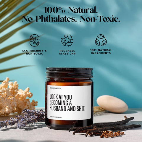 9oz amber glass jar candle with label “Look at You Becoming a Husband and Shit” displayed alongside text showcasing eco-friendly & non-toxic, reusable glass jar, and 100% natural ingredients, making it a sustainable yet funny wedding gift.