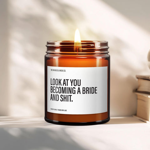 Close-up of a 9oz amber glass jar candle with black metal lid, white label reading “Look at You Becoming a Bride and Shit” in bold black text, styled on a neutral background with warm lighting, perfect for funny bridal gifting.