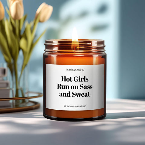 Close-up of a 9oz amber glass jar candle with black metal lid, white label reading “Hot Girls Run on Sass and Sweat” in bold black text, styled on a neutral background with warm lighting, perfect for funny running gifts.
